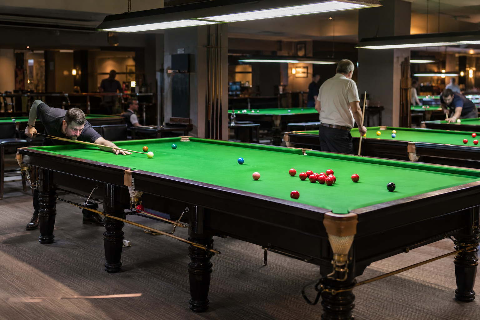 Players at several full-size green snooker tables in an indoor club